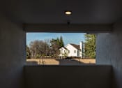 Thumbnail 56 of 61 - A white house is seen through a window in a room with concrete walls.