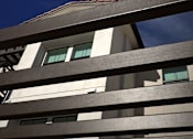 Thumbnail 51 of 61 - A building with a white facade and dark brown slats in the foreground.