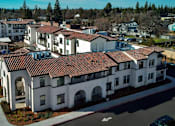 Thumbnail 17 of 61 - A large white building with a red tile roof is surrounded by smaller buildings and trees.