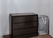 Thumbnail 115 of 127 - A brown chest of drawers sits next to a white bag in a room with a white wall and a white shelf.
