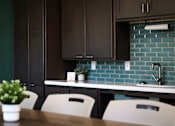 Thumbnail 45 of 127 - A kitchen with a table and chairs in front of a counter with a plant on it.