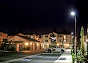 Thumbnail 99 of 117 - A large building with a parking lot in front of it is lit up at night.