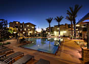 Thumbnail 2 of 45 - A pool area with lounge chairs and palm trees at night.
