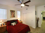Thumbnail 11 of 45 - A bedroom with a red bedspread and a ceiling fan.