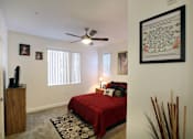 Thumbnail 12 of 45 - A bedroom with a red bedspread and a ceiling fan.