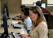 Thumbnail 1 of 126 - A woman and a boy are using computers in a room with other people.