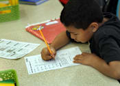 Thumbnail 6 of 126 - A young boy is writing on a piece of paper with a pencil.