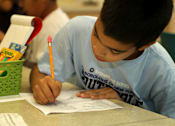 Thumbnail 10 of 126 - A boy is writing on a piece of paper with a pencil.