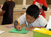 Thumbnail 7 of 126 - A boy is writing on a green piece of paper.