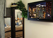 Thumbnail 47 of 126 - A black TV is mounted on a wall above a bed with a grey curtain.