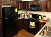 Thumbnail 24 of 126 - A black refrigerator stands in a kitchen with wooden cabinets and a black stove.