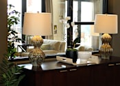 Thumbnail 46 of 126 - Two table lamps with white shades on a table with a vase and a plant.