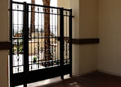 Thumbnail 116 of 126 - A black gate with a design on it is in the foreground of a photo showing a patio with a palm tree in the background.