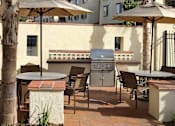 Thumbnail 88 of 126 - A patio with a grill and chairs under umbrellas.