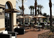 Thumbnail 86 of 126 - A patio with tables and chairs and palm trees.