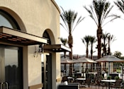 Thumbnail 69 of 126 - A patio with tables and chairs and palm trees in the background.