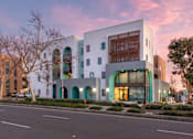 Thumbnail 13 of 16 - A modern building with a white facade and a large glass window is surrounded by trees.