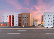 Thumbnail 8 of 16 - A white car is parked in front of a white building with a red arch.