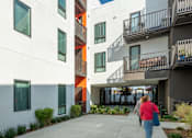 Thumbnail 14 of 16 - A woman walks down a concrete walkway between two buildings.