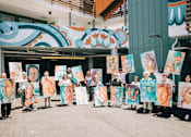 Thumbnail 3 of 11 - A group of people holding up paintings of women's faces.