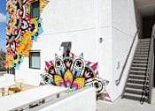 Thumbnail 1 of 17 - A white building with a staircase and a mural on the wall.