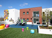 Thumbnail 10 of 17 - A playground area with a slide and a building in the background.
