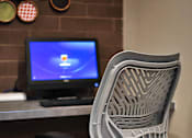 Thumbnail 78 of 94 - A white chair with a blue cushion is in front of a computer monitor.