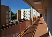 Thumbnail 29 of 94 - A long corridor with a metal railing on the left side and buildings on the right.