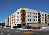 Thumbnail 22 of 94 - A white building with orange balconies and a parking lot in front.