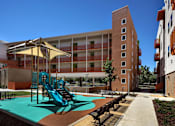 Thumbnail 4 of 94 - A playground with a slide and a bench in front of a building.
