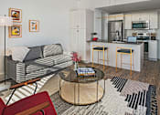 Thumbnail 9 of 10 - A modern living room with a grey couch, a coffee table, and a kitchen in the background.