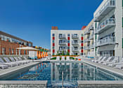 Thumbnail 32 of 32 - A large pool in front of apartment buildings with sun loungers on either side.