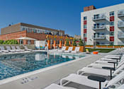 Thumbnail 29 of 32 - A pool with chairs around it and a building in the background.