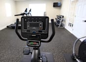 Thumbnail 7 of 20 - A black exercise bike with a digital screen in a room with a white door.
