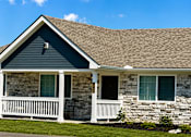 Thumbnail 5 of 42 - An apartment building with blue siding and rock with a porch that has white railings.