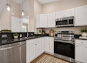 Thumbnail 18 of 42 - A kitchen with white cabinets and black countertops.