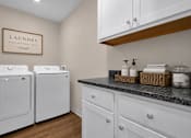 Thumbnail 42 of 42 - A laundry area with a washer and dryer and white cabinets with a black counterop.