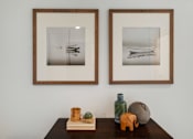 Thumbnail 11 of 39 - a wall with two framed pictures and a wooden table with various objects on it