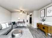 Thumbnail 8 of 15 - A living room with a grey couch, a coffee table, and a ceiling fan.
