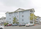 Thumbnail 14 of 15 - A grey building with cars parked in front.