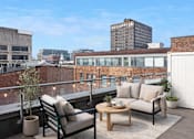 Thumbnail 6 of 10 - A balcony with a chair, couch, and table with a view of the city.