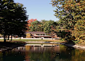 Thumbnail 3 of 15 - A serene landscape with a house, trees, and a pond.