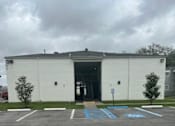 Thumbnail 3 of 3 - A white building with a grey roof and a parking lot in front.
