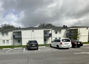Thumbnail 2 of 3 - A parking lot in front of a white apartment building with cars parked.