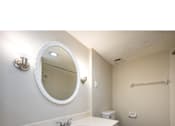 Thumbnail 12 of 17 - A bathroom with a white sink and a round mirror.