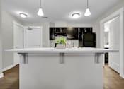 Thumbnail 8 of 25 - A white kitchen island with a plant on top and a black fridge in the background.