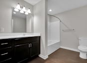 Thumbnail 18 of 25 - A white toilet sits in a bathroom with a white sink and a mirror.
