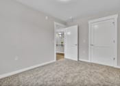 Thumbnail 6 of 25 - A room with white walls and a carpeted floor with two white doors.