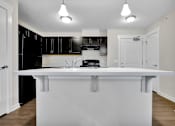 Thumbnail 15 of 25 - A white kitchen island with a black fridge and microwave.