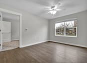 Thumbnail 21 of 25 - A room with a ceiling fan and a window with a view of trees.